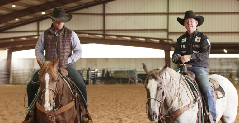 Trevor Brazile and Miles Baker mounted on horses in an indoor arena.